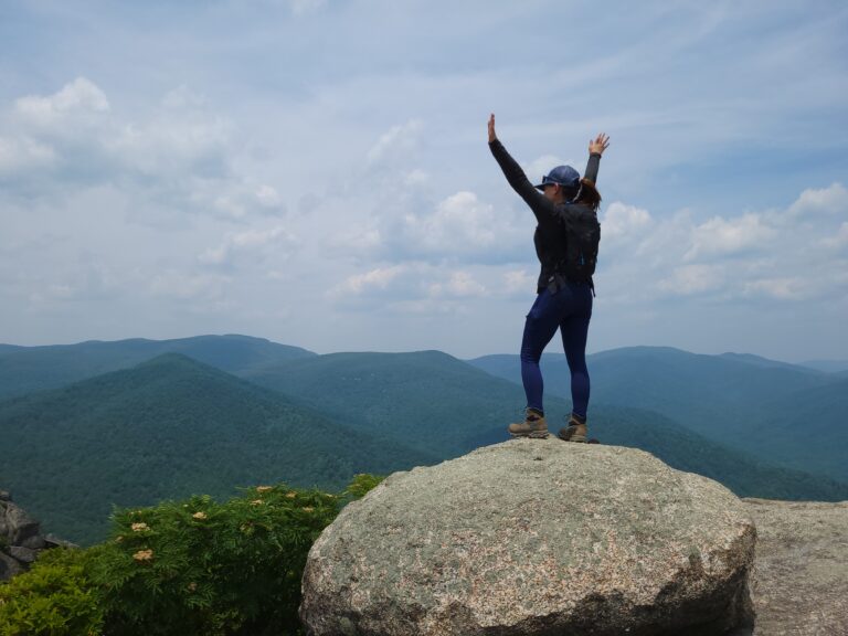 Roxy is doing her summit pose with her arms up in the air on the top of Old Rag.
